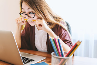 woman working on laptop biting pencil in frustration