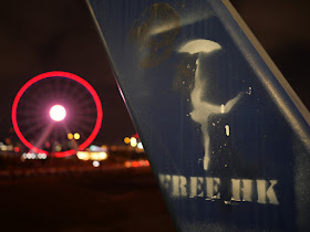 graffiti of "FREE HK" and dancer holding an umbrella with the Hong Kong Observation Wheel lit up in red in the background at night