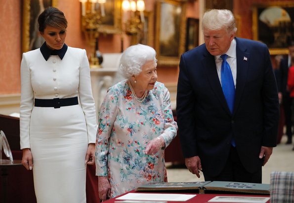 Melania Trump is wearing a custom white crepe dress with navy details by Italian fashion house, Dolce & Gabbana. Queen Elizabeth