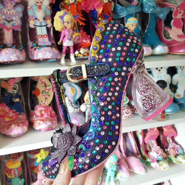 Irregular Choice shoe in hand with jewelled uppers and seahorse detail in front of shelves of shoes