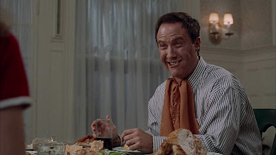Thinner 1996 movie still showing Robert John Burke laughing loudly as he shovels food into his face at his dining room table