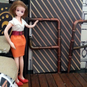 One-twelfth scale Takara compact doll in a modern miniature scene, pointing at two pipe shelving units.