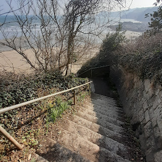 Steep granites steps leading down to a sandy beach. Edged by steep cliffs. Sunny day.