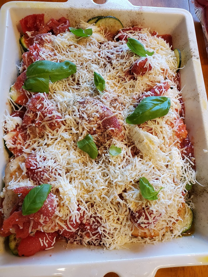 this is a casserole pan with chicken topped with cheeses tomato and zucchini