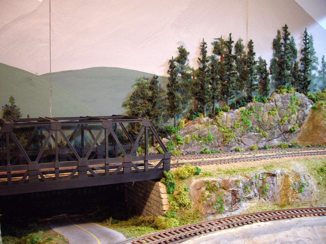 Background terrain and forest scene under construction around an upgraded warren-truss bridge