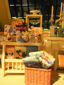 Modern miniature shabby chic shop display of sheets towels, cake stands and toiletries on cream shelves.