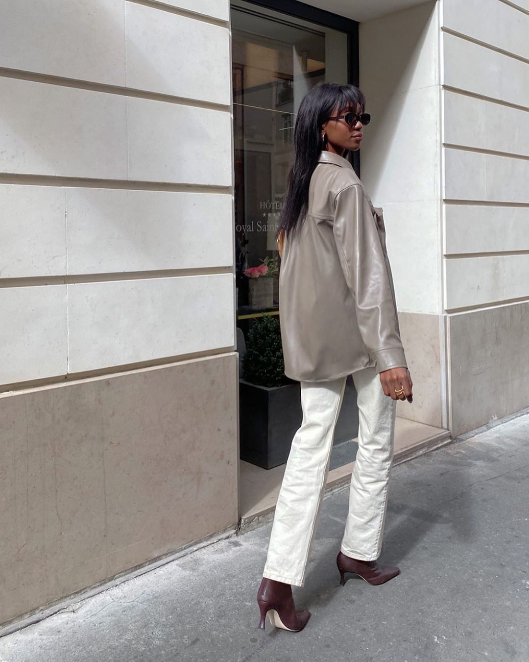 Fall Outfit Idea — @emmanuellek_ in black oval sunglasses, a neutral leather shirt, white jeans, and brown boots