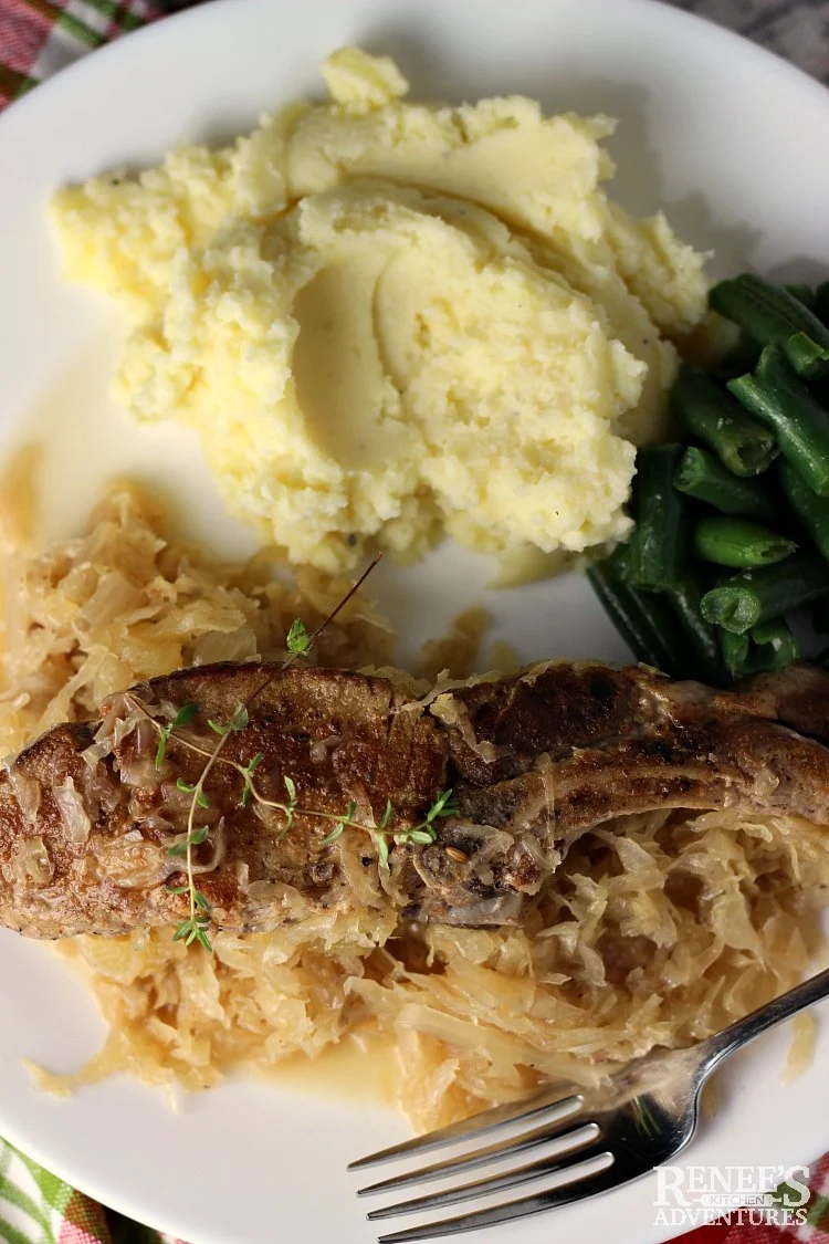 Overhead view of one serving of Country Style Ribs with Sauerkraut by Renee's Kitchen Adventures with mashed potatoes and green beans on a white plate