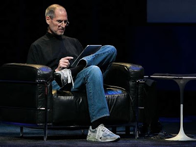 Steve Jobs sitting in a chair looking at a tablet