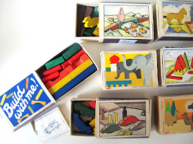 Seven sets of miniature vintage wooden blocks packaged in matchboxes, with one matchbox (with 'build with me' printed on the lid) open to show tiny blocks and an instruction sheet.