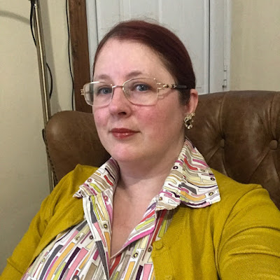 A redheaded woman in a mustard cardigan and 70s-print shirt with a huge collar.