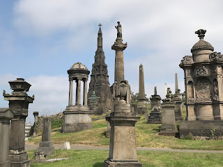 A photo of the view to top of Glasgow Necropolis with lots of ornate tombs and a statue of  John Knox in the distance.  Photo by Kevin Nosferatu for The Skulferatu Project.