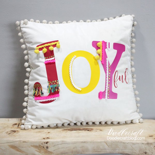 Make a joyful pom-pom pillow inspired by Anthropologie in this fun and simple tutorial. Using brightly colored iron-on vinyl and colorful trims and pom-poms to make the Joy pop!