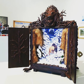 Small wooden cupboard decorated with Narnia-themed items, on display in an art gallery.