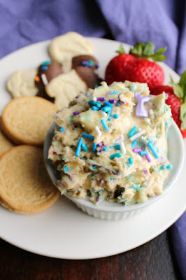What could be more fun than a dessert dip that tastes like cookie dough? One that is filled with sprinkles of course! This birthday cookie dough dip is begging to be eaten with your favorite dippers! ramekin of birthday cookie dough dip with extra sprinkles on top on small plate with berries, animal crackers and oreo dippers