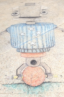 A chalk drawing of Robot Sam, the Maker Faire mascot on the floor of the venue. Sam has a hexagonal head like a bolt on a screw, a cylindrical body (blue) a red torso, bracket legs which hold a pencil horizontally. A ball of yarn is wound around the pencil. The southern cross constellation is on Sam's front to signify that Maker Faire Adelaide is in the Southern Hemisphere.