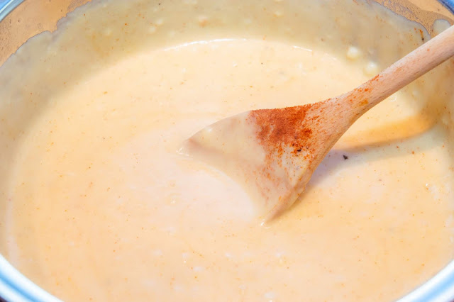 A creamy paprika coloured sauce with a wooden spoon laying inside.