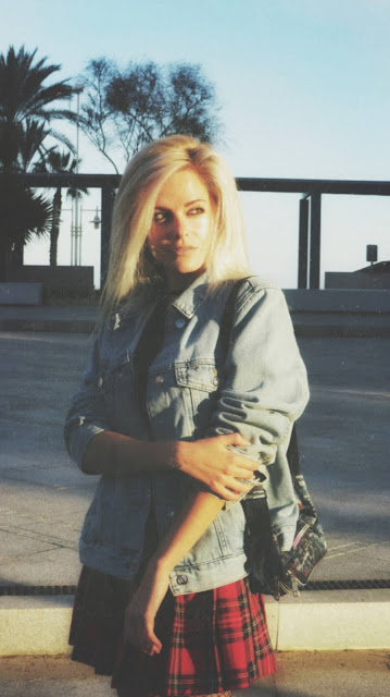 Estilo grunge con camiseta negra, falda de tablas tartán, medias de red grande, botas estilo militar y cazadora vaquera