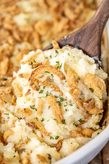 Mashed Potato Casserole - great make ahead side dish for the holidays! SO easy and tastes AMAZING!!! Instant mashed potatoes, hash browns, cream cheese, butter, Monterey Jack cheese, sour cream, garlic, salt, pepper, and french fried onions. Can make in advance and refrigerate or freeze for later. Great for a crowd! #thanksgiving #casserole #makeahead #freezermeal #christmas scooping mashed potatoes from casserole dish