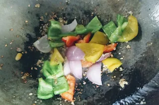 Sauteed onions capsicum red yellow bell peppers in a wok for chilli paneer recipe