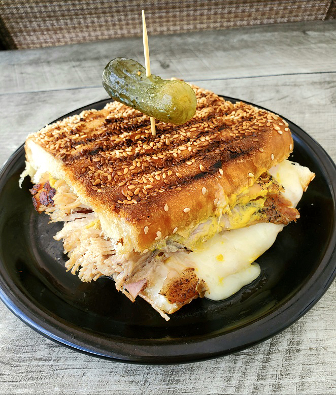 Cubano Pork Sandwich this is cuban sandwich with roasted pork, ham, cheese, mustard on a black dish and pickle on top
