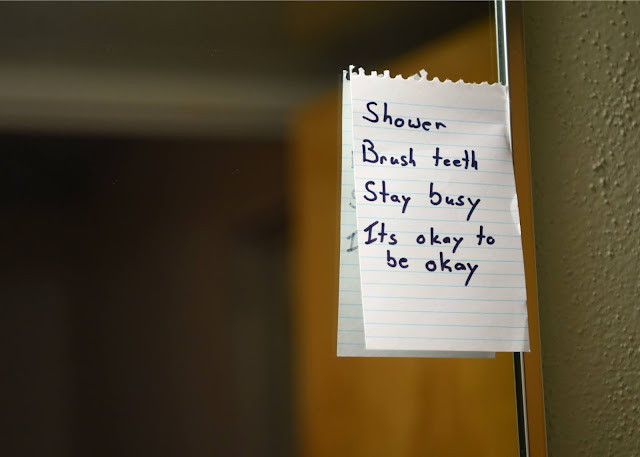 A piece of paper on a mirror that reads "Shower, Brush teeth, Stay busy, Its okay to be okay."