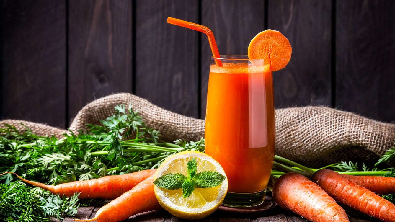 Suco de Laranja com Cenoura e Limão Um copo de suco próximo a laranjas e cenouras
