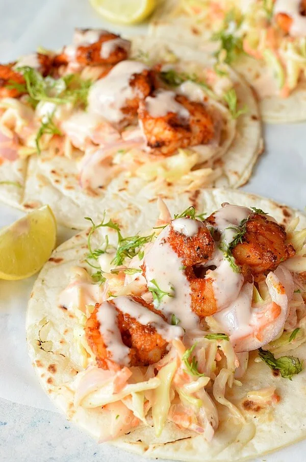 a white background with tortilla topped with cabbage cilantro lime slaw and spicy shrimp topped  with sriracha sauce