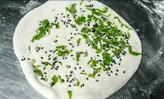 Rolled paneer kulcha dough topped with black sesame seeds and chopped coriander leaves