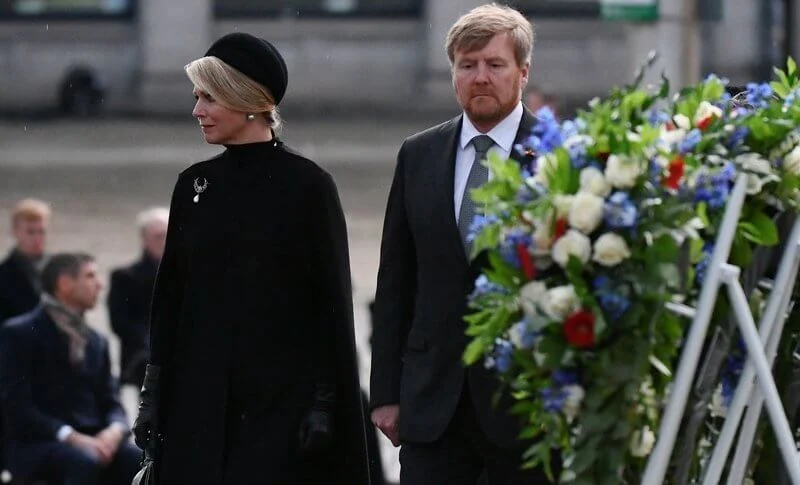 Queen Maxima wore a black wool high collar cape coat. Black leather handbag. Pearl drop earrings and diamond brooch. Gripoix earrings