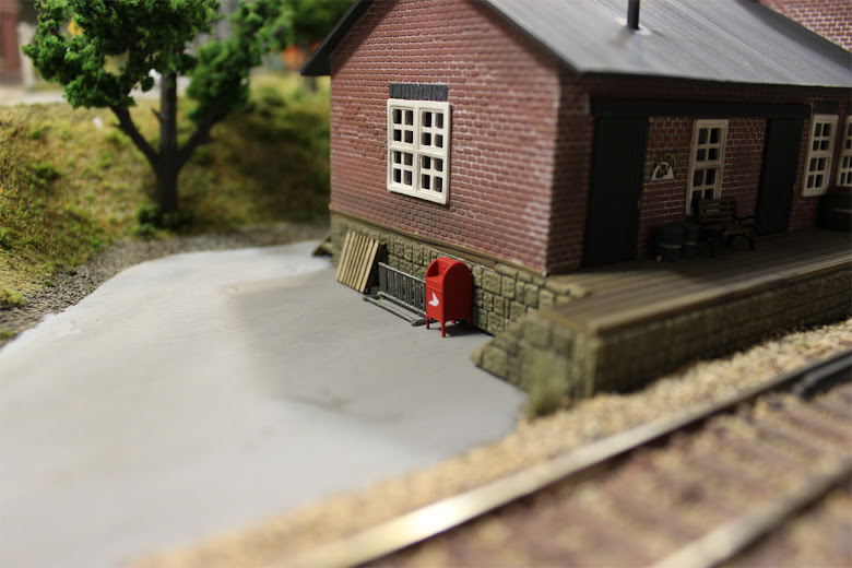 Wooden pallet, mail box, and bike rack up against the foundation of a POLA freight station kit