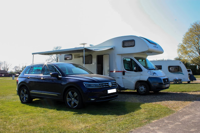 Photo of a motorhome with awning up and a car in front.
