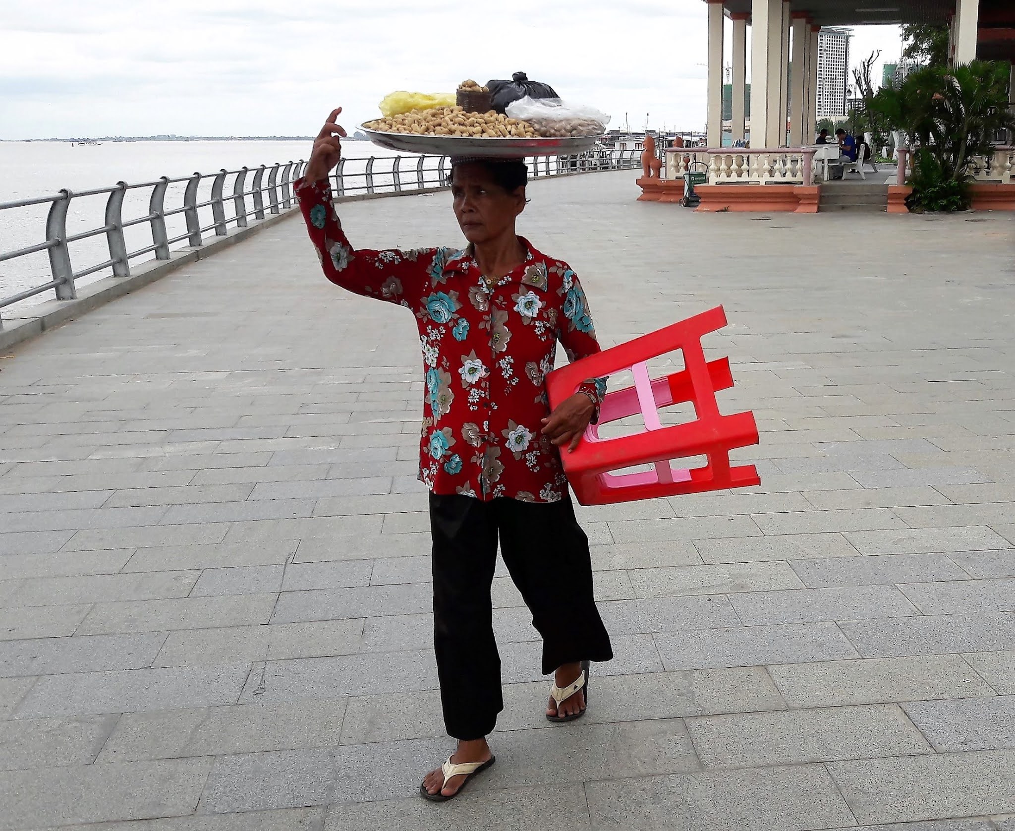 A female vendor walking on the Riverside Path carrying a tray full of nuts on her head