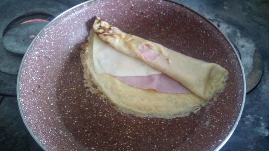 Enrollando en la sartén los crepes salados rellenos de jamón york y queso.