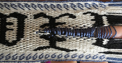 A photo of a section of tablet woven band with the warp threads pulled to either side and the weft exposed