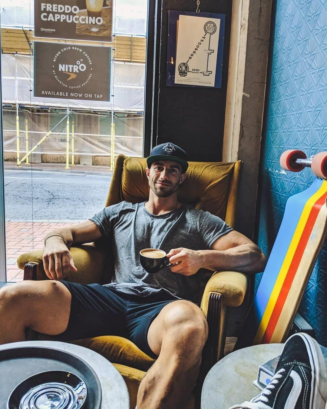 hunky-local-dilf-drinking-coffee-shop-strong-huge-muscle-legs-smirk-smiling-face-baseball-cap-chillin