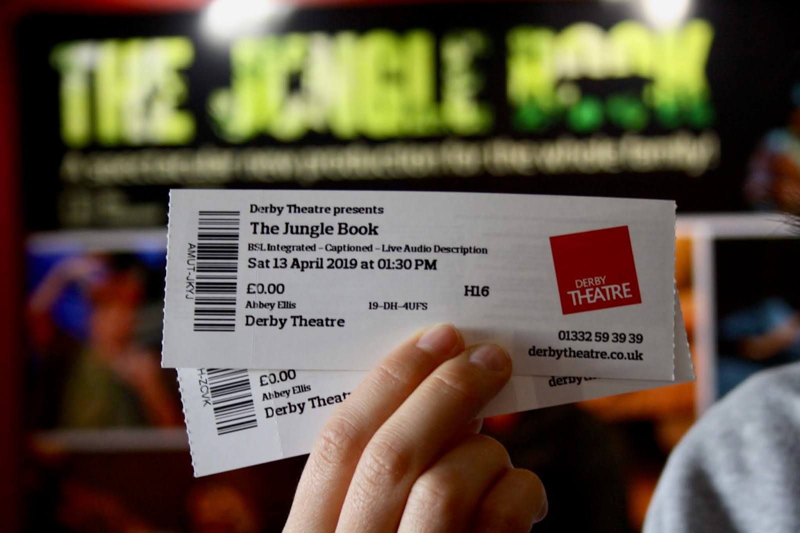 Two tickets to The Jungle Book at Derby Theatre, held up in front of a poster for the performance