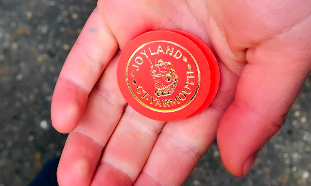 A close up of a hand holding some orange Joyland ride tokens