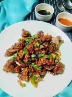 Serving chicken manchurian in a plate, soya sauce and red chilly sauce in background