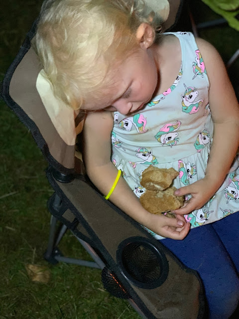 3 year old asleep in a camping chair cuddling a roll of bread
