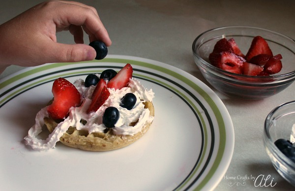 child adding blueberries to waffle