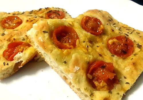 Una especie de pizza con tomates cherry y hierbas aromáticas
