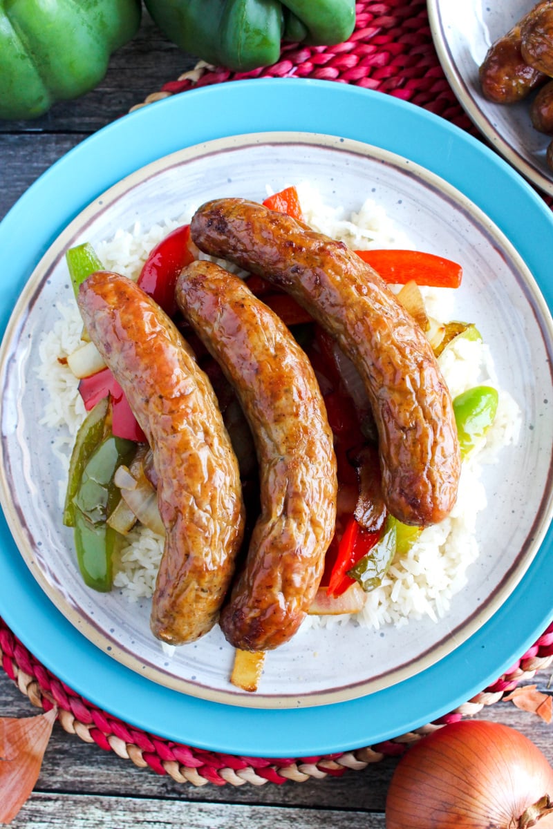 Top view of Air Fryer Sausages over rice, peppers, and onions on a tan and blue plate.