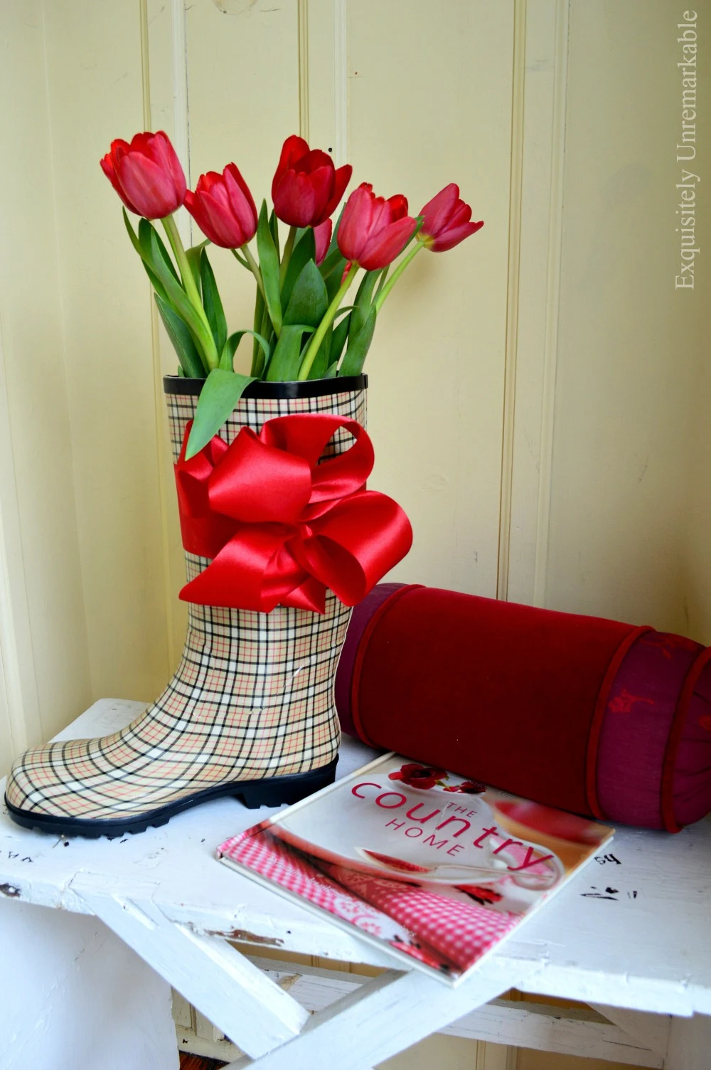 Red tulips in a plaid rain boot on a stool