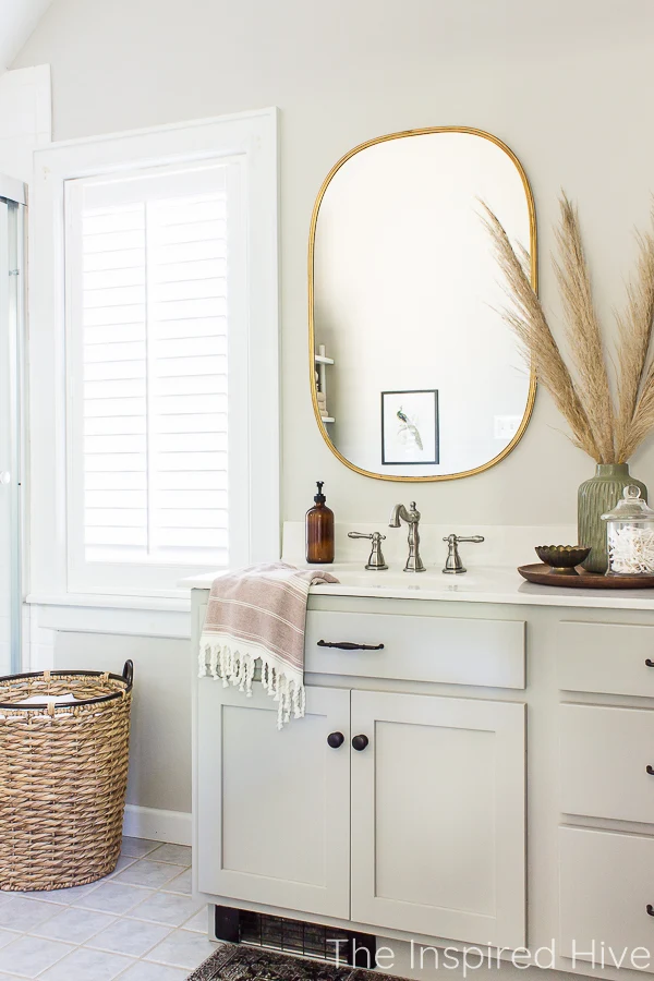 Master bathroom with grey vanity, gold mirror, nickel faucet, plantation shutters, and hyacinth basket laundry hamper