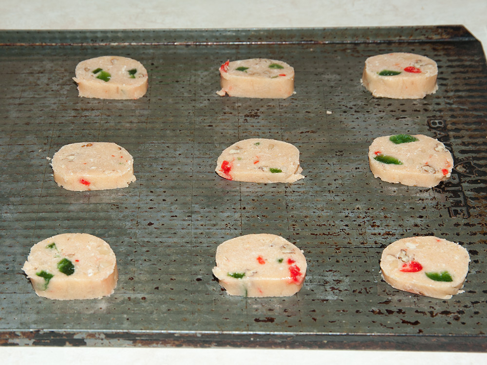Cherry nut cookie dough sliced into rounds and placed on cookie sheet, ready to bake.
