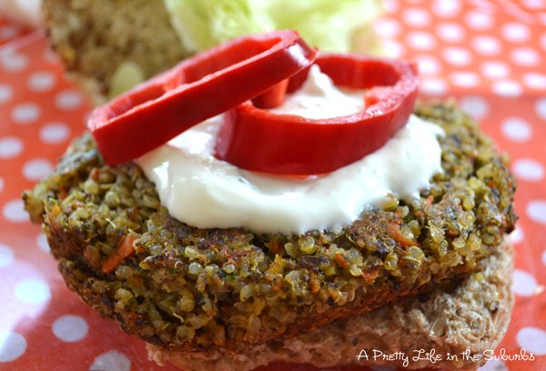 a side view of a cooked quinoa burger topped with tzatziki and sliced red peppers