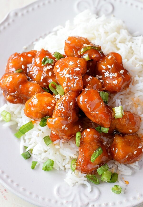 fried sweet and sour chicken with sesame seeds and spring onion chopped served on top of rice