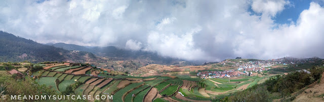 It is a panoramic view of Poombarai Village with colourful village in right and farms in right and a school on extreme right on top