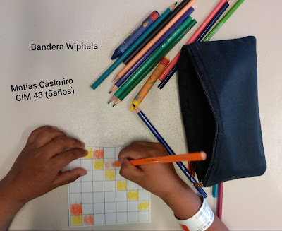 Foto en donde se observa las manos de un niño pintando la bandera Wiphala con lápices de colores. En la imagen dice Bandera Wiphala. Matías Casimiro. CIM 43. 5 años